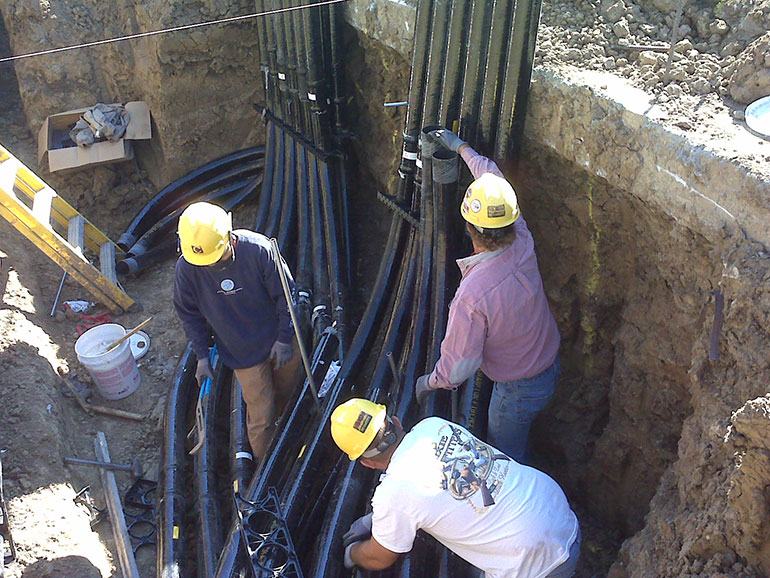 Workers install electrical conduit underground.