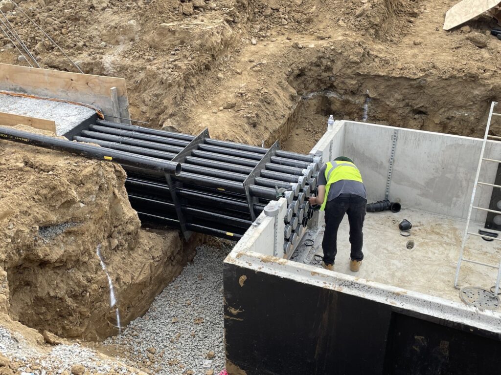 An installer checks a fiberglass conduit duct bank at an industrial construction job site.