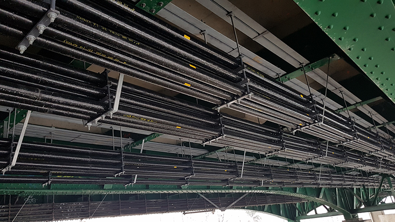 Fiberglass electrical conduit hangs under a bridge